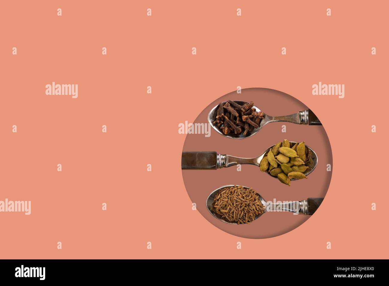 selection assorted indian spices cumin seeds cardamom cardamon pods cloves display on spoons on a colorful colourful peach background Stock Photo
