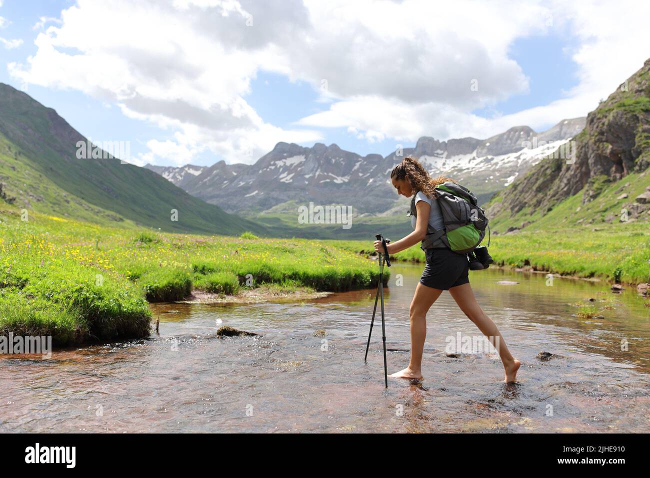 Side view portrait of a barefeet hiker crossing a river in the mountain Stock Photo