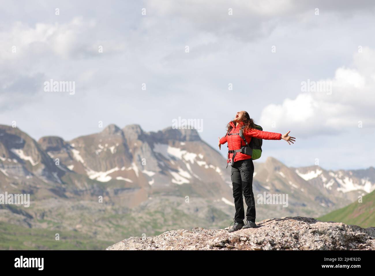 Excited hiker in red outstretching arms screaming in a high mountain Stock Photo
