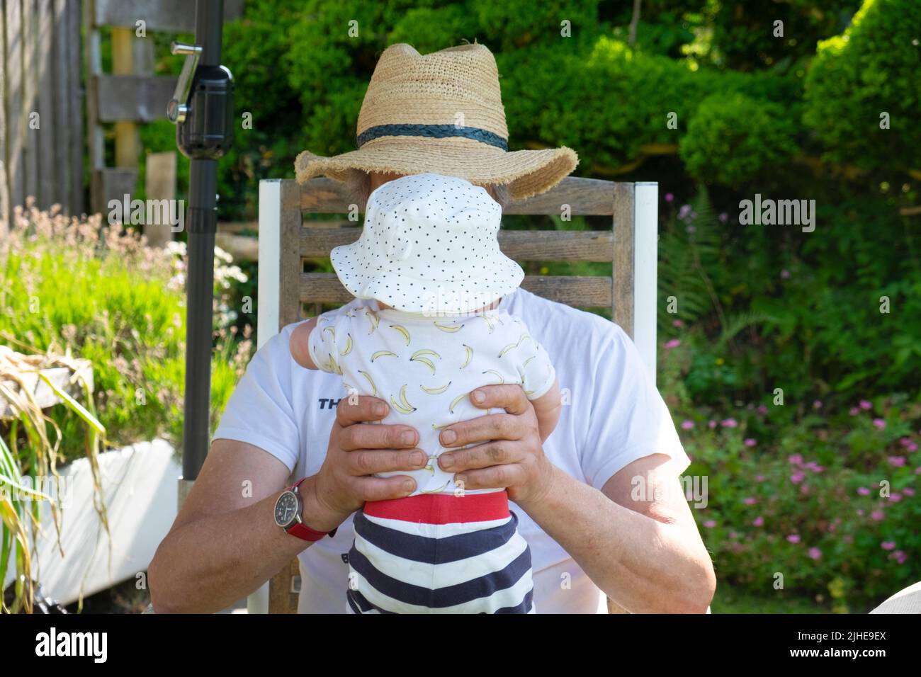 Granddad and grandchild little baby back view wearing sunhat sitting in the shade in the garden on 18 July 2022 in heatwave Wales UK   KATHY DEWITT Stock Photo