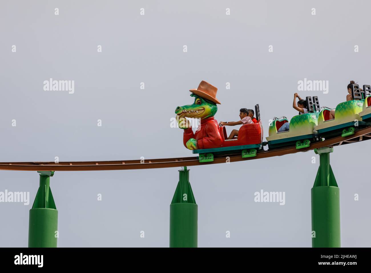 Southend-on-Sea, UK  July 17th 2022  Children on a roller coaster with crocodile cartoon character lead car. Isolated against clear sky background. Gr Stock Photo