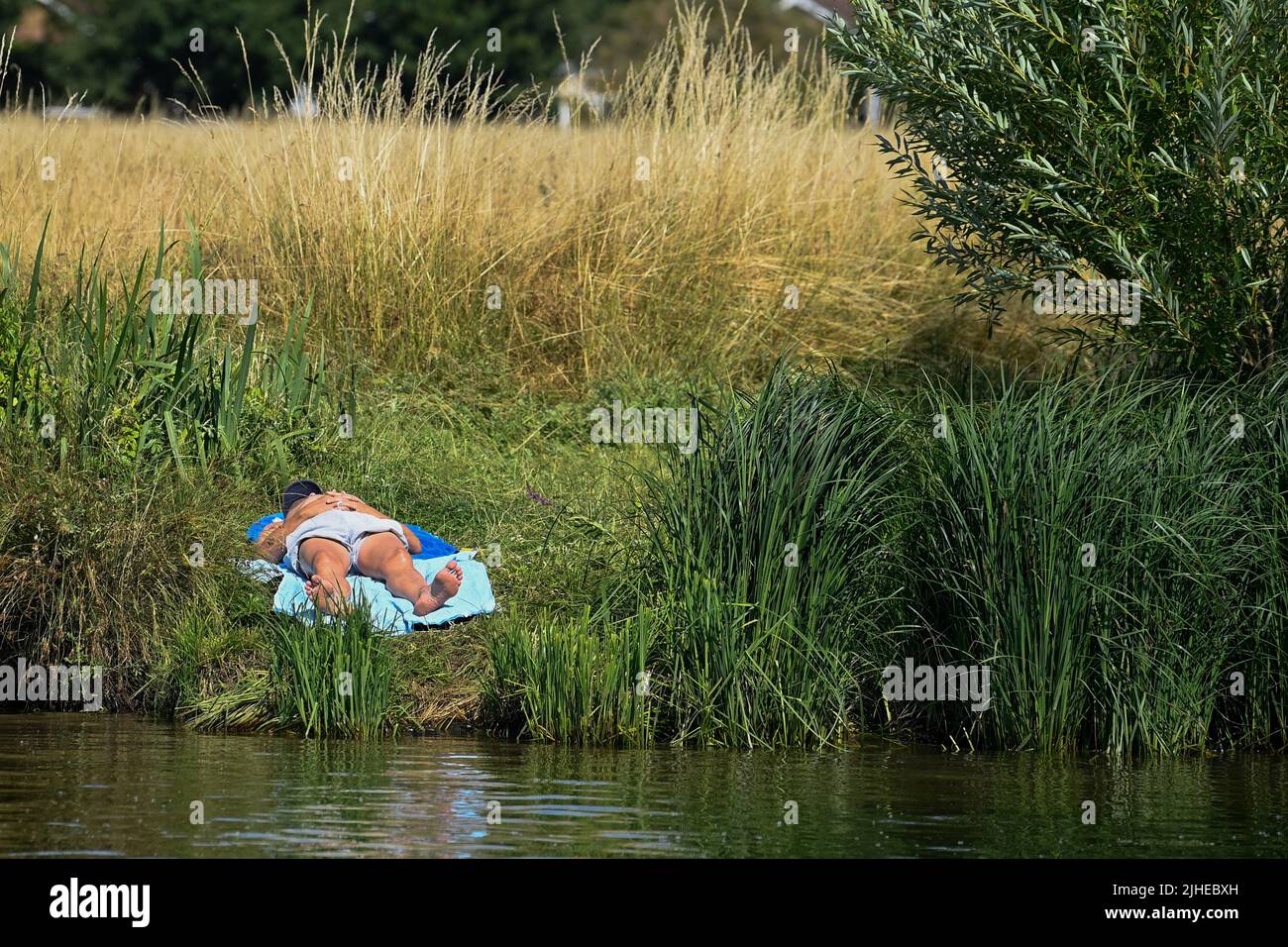 A person sunbathes next to the River Thames during the hot weather, near Windsor, Britain, July 18, 2022. REUTERS/Toby Melville Stock Photo