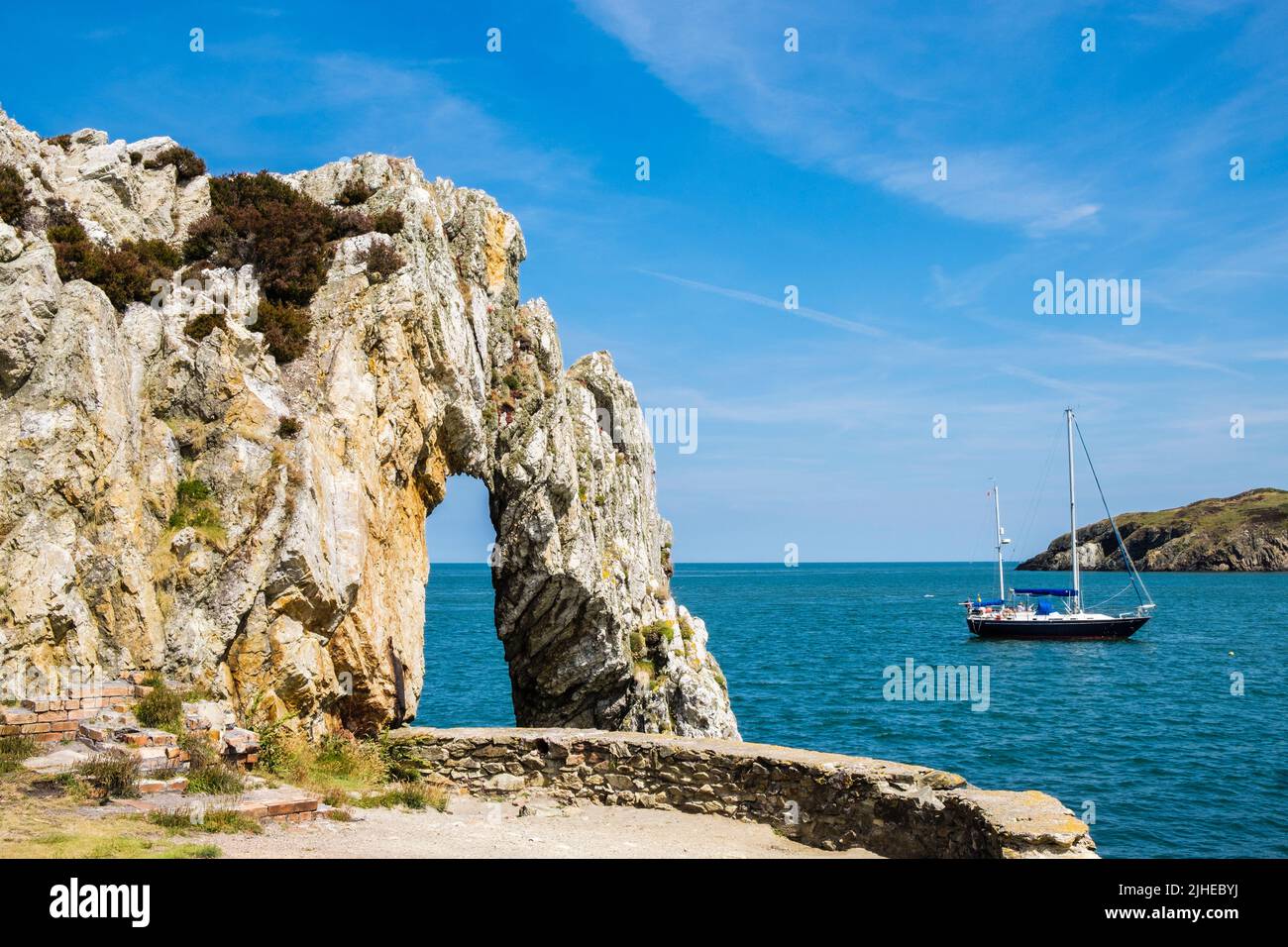 Natural white rock arch with sailboat in the bay at Porth Wen between Cemaes and Amlwch on Isle of Anglesey, Wales, UK, Britain Stock Photo