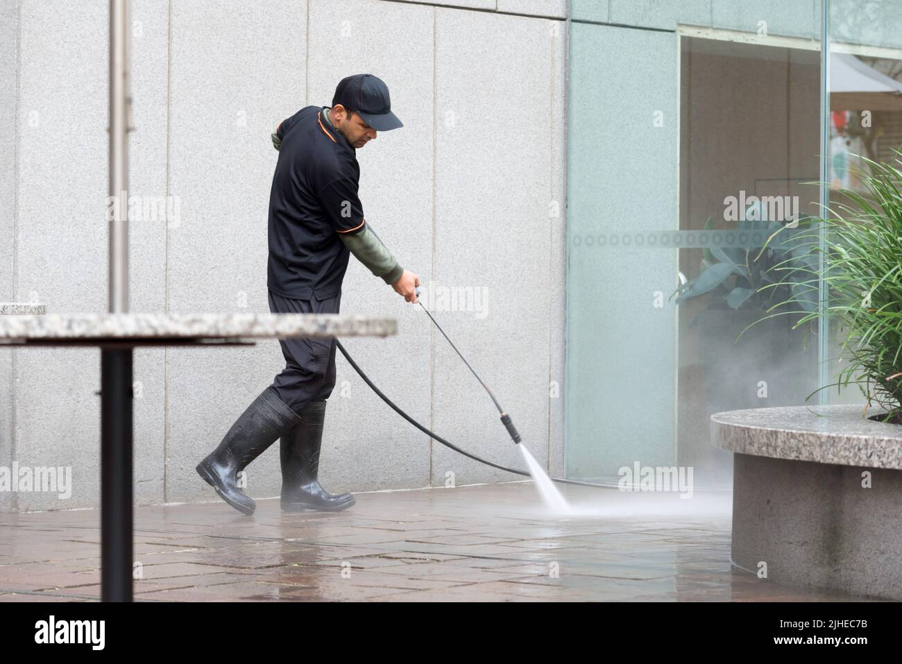 A man using a high-pressure hose to clean a paved courtyard at the Australia Square complex in Sydney, New South Wales Stock Photo