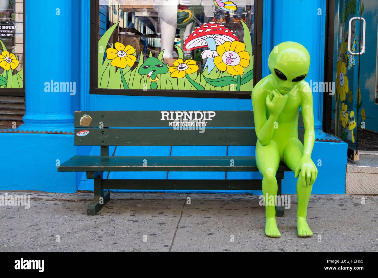 An alien sitting on a bench outside Ripndip, a clothing storewith a motto We Out Here Alien Products From RIPNDIP. On Broadway in Manhattan. Stock Photo
