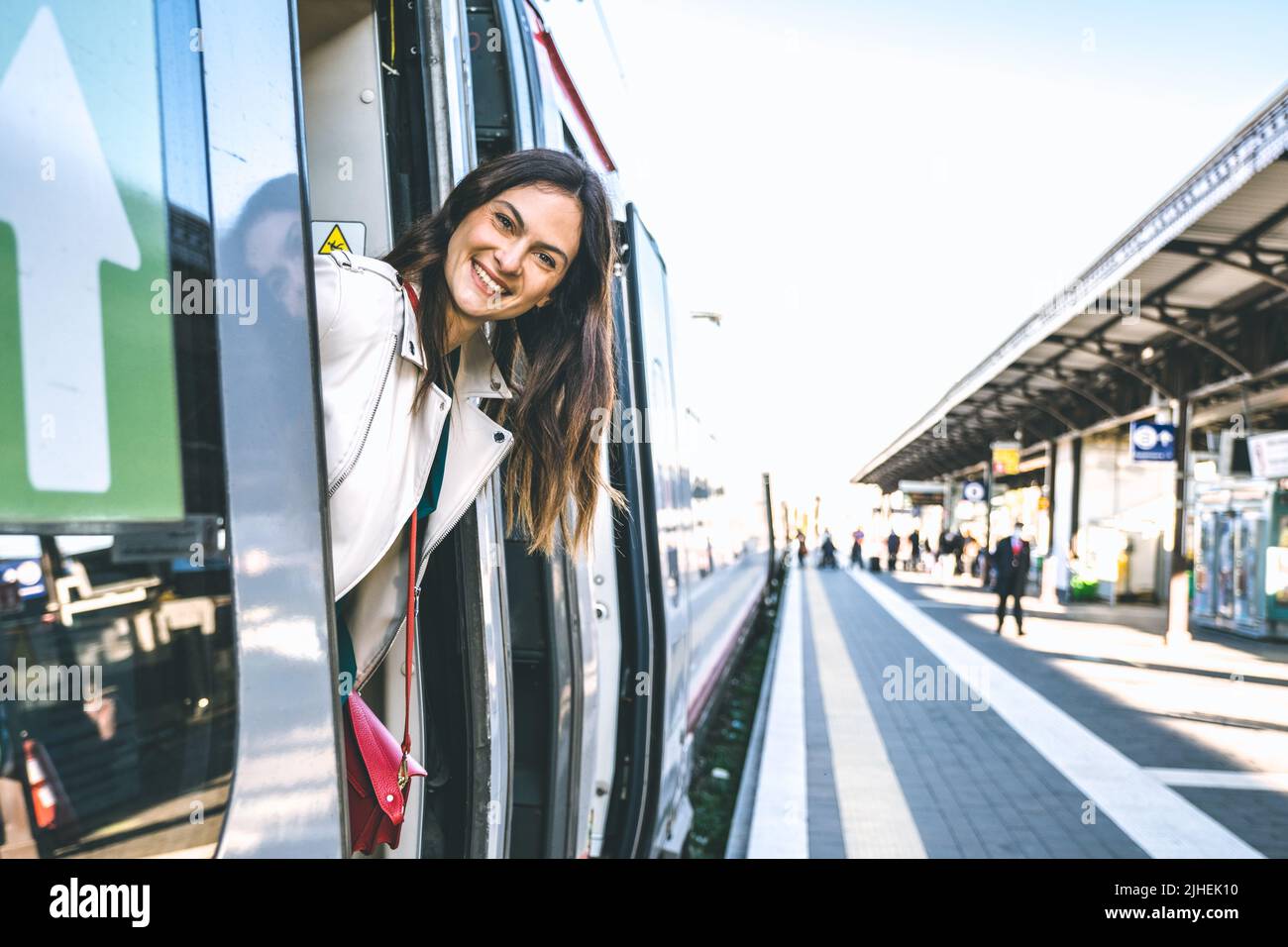 Young business woman standing on train door peeking out looking for somebody in railway station - Potrait of beautiful traveler woman getting Stock Photo