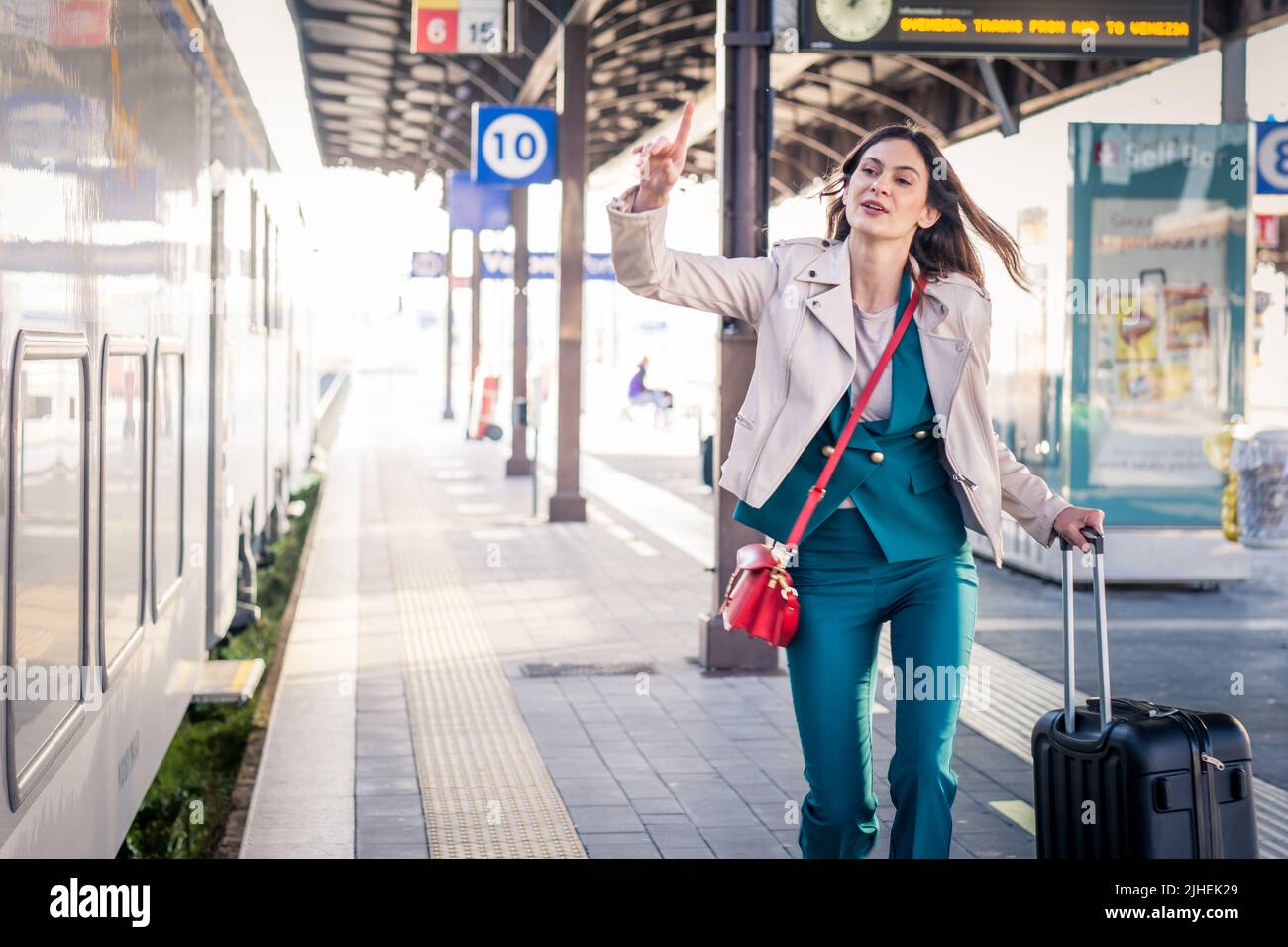 Beautiful girl running and chasing the leaving train in station. Waving hand and rushing to get on - Young business woman with suitcase running Stock Photo