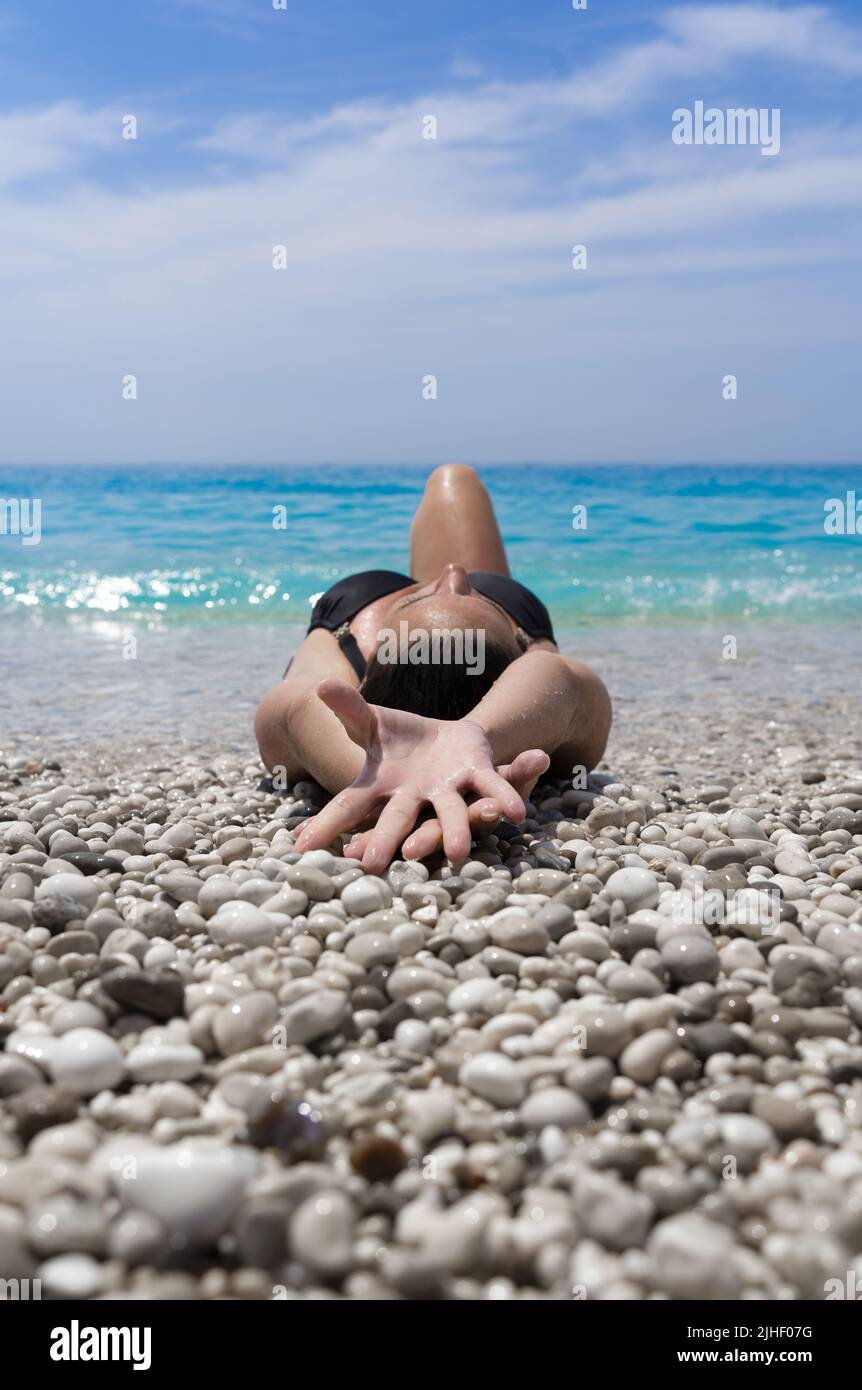 Attractive woman resting with outstretched arms on a beautiful pebble beach Stock Photo