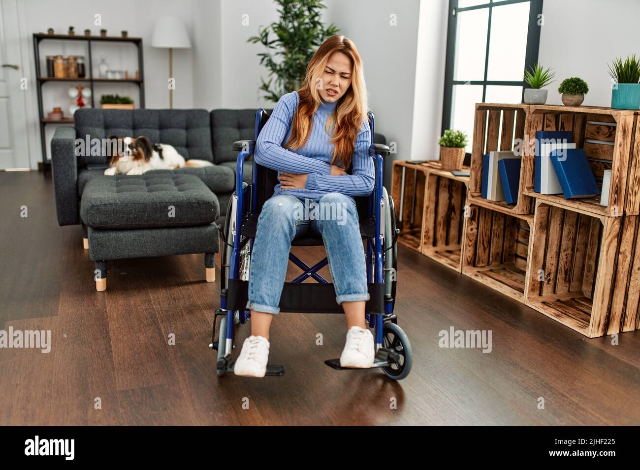 Young beautiful woman sitting on wheelchair at home with hand on