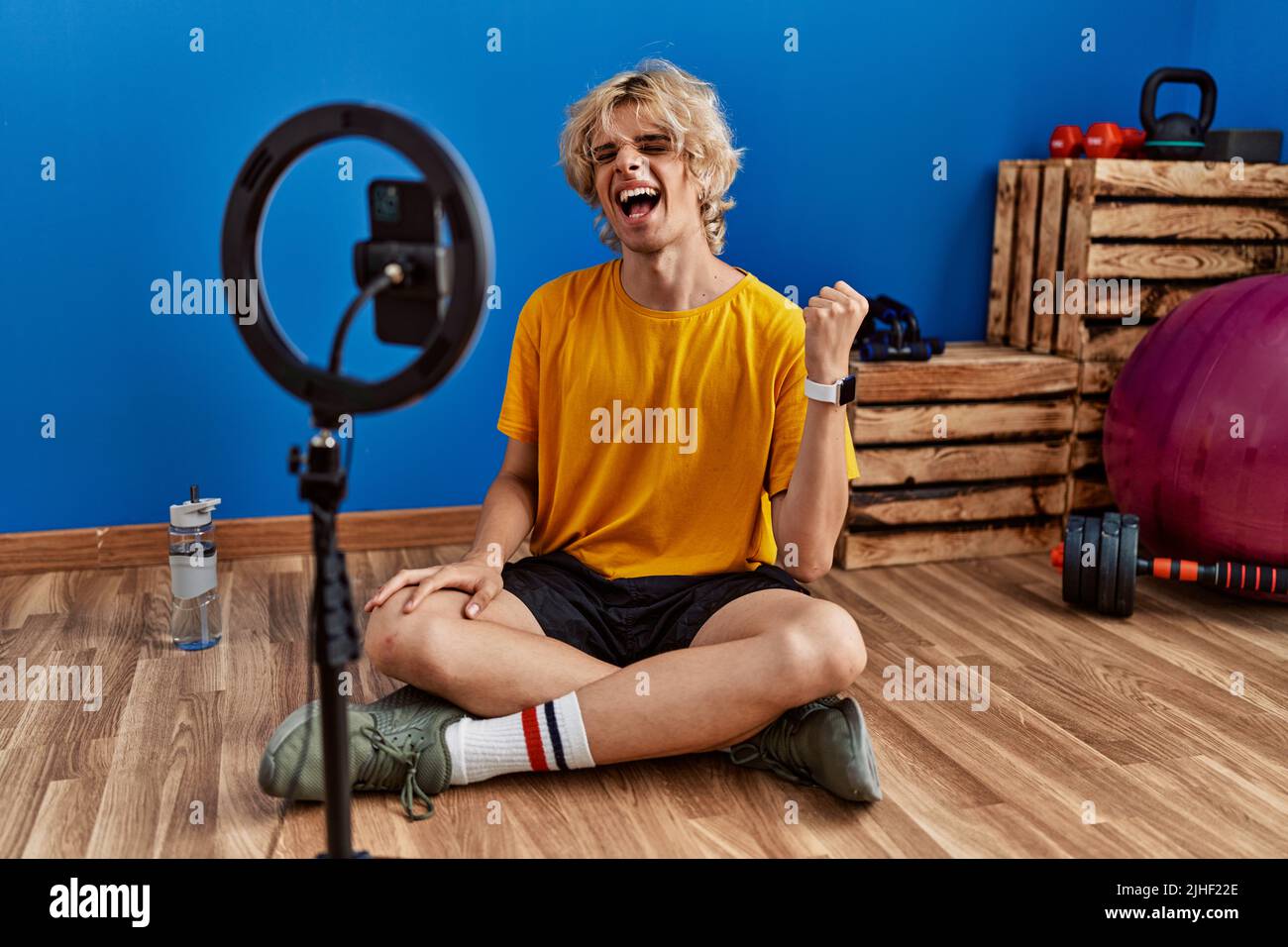Young man recording training tutorial at the gym screaming proud
