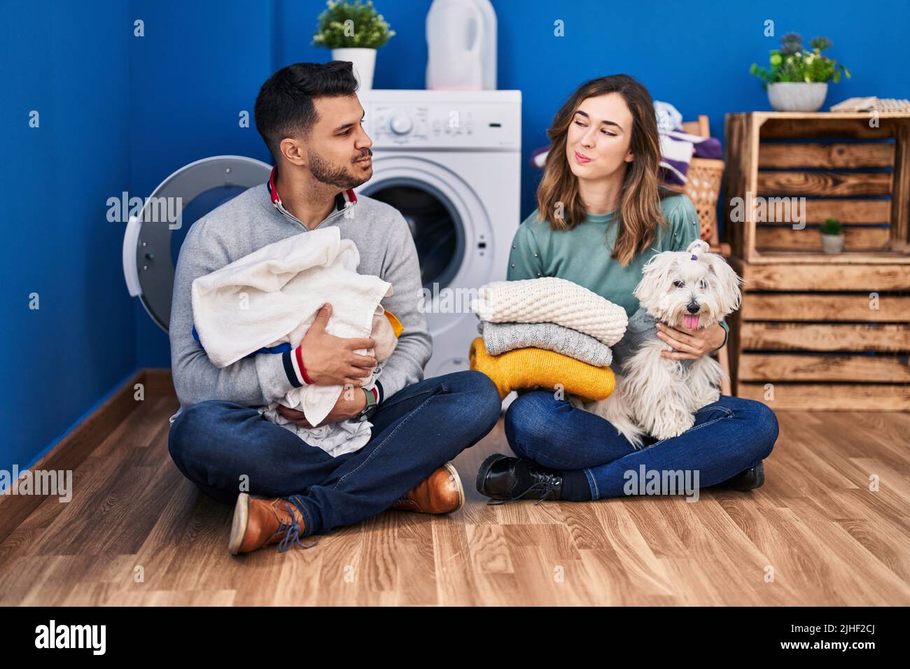 Young hispanic couple doing laundry sitting on the floor smiling ...