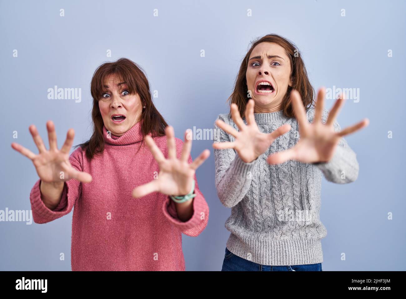 Mother and daughter standing over blue background afraid and terrified with fear expression stop