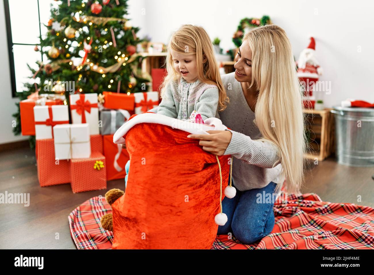 Mother and daughter holding gifts on christmas bag sitting on the floor