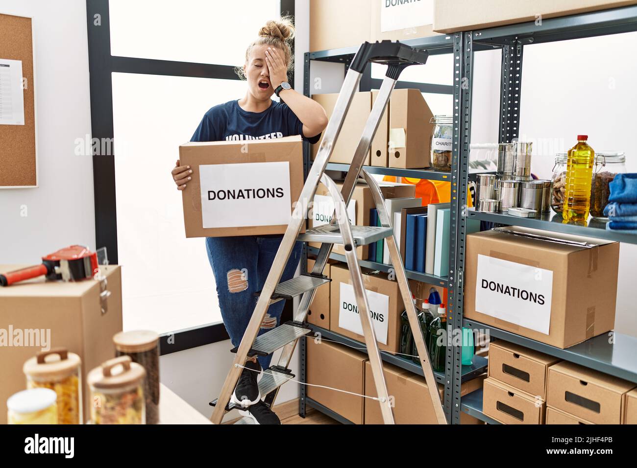 Young caucasian woman volunteer holding donations box yawning tired