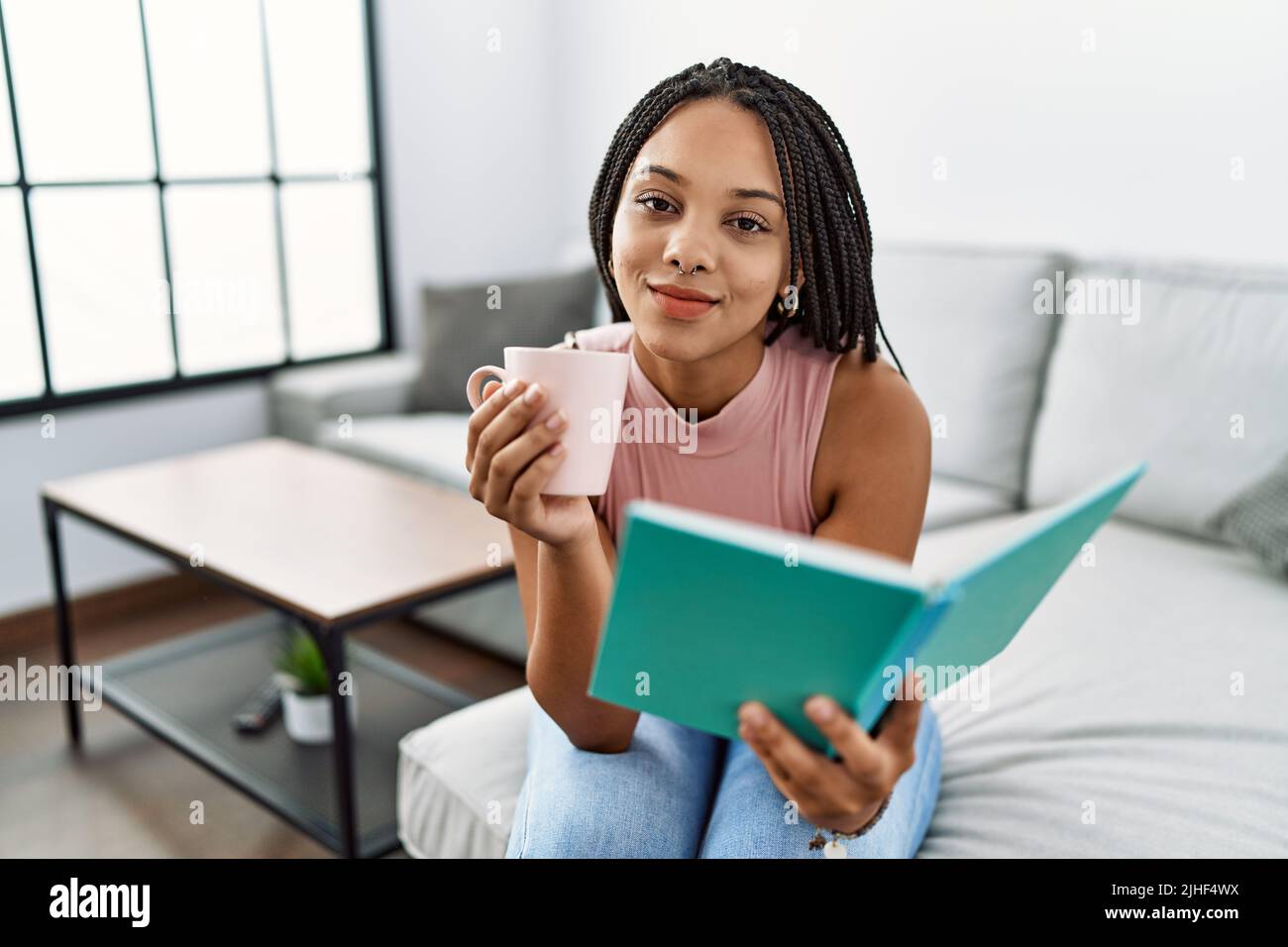 Young african american woman reading book and drinking coffee at home ...