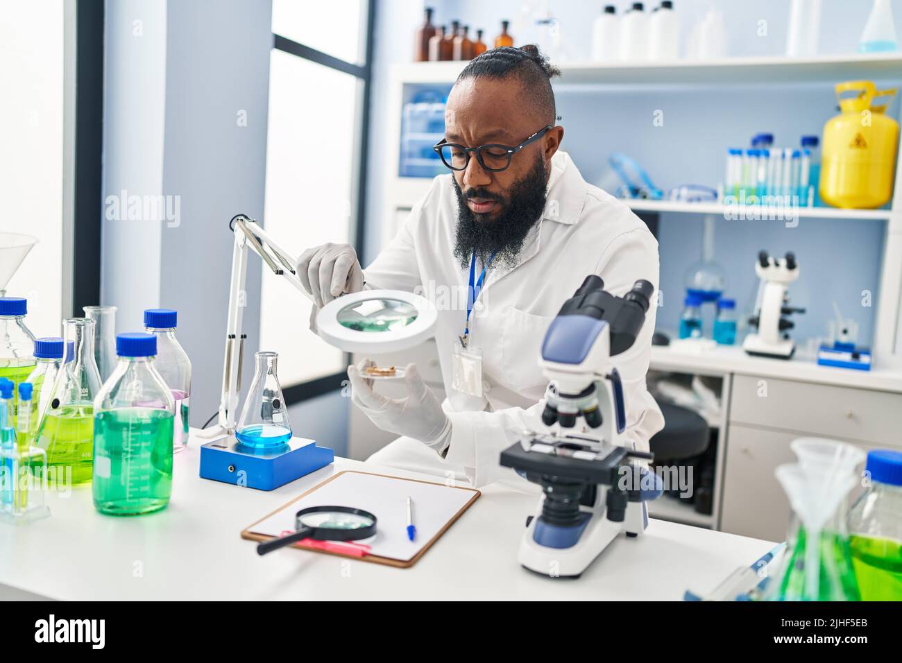 Young african american man wearing scientist uniform using loupe at
