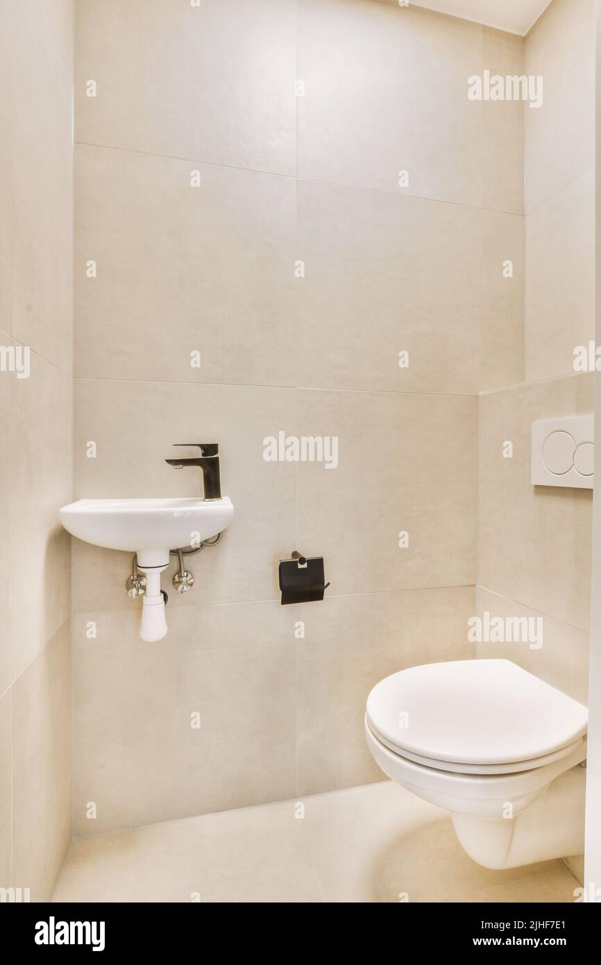 Interior of narrow restroom with sink and wall hung toilet with white