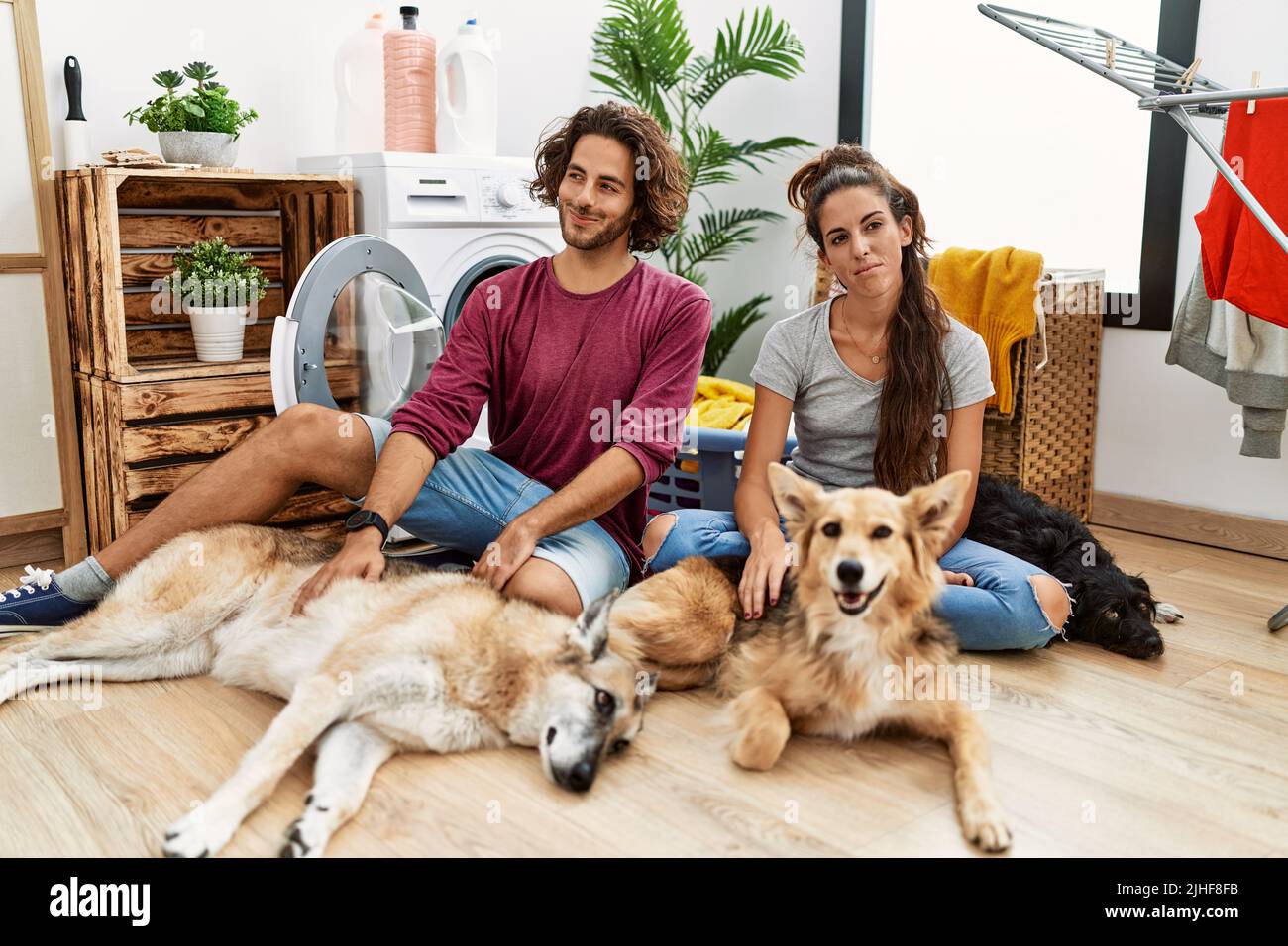 Young hispanic couple doing laundry with dogs smiling looking to the ...