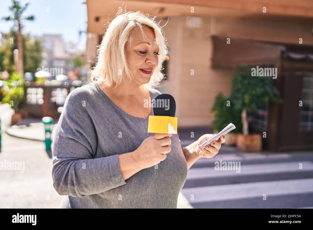 Middle age blonde woman reporter working using microphone at street ...
