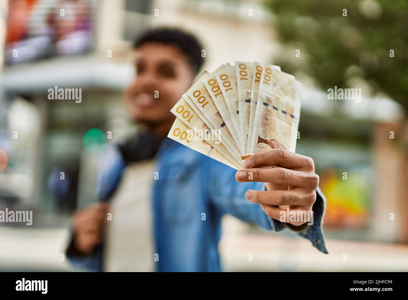 Hispanic young man holding 100 danish krone baknotes at the street Stock Photo