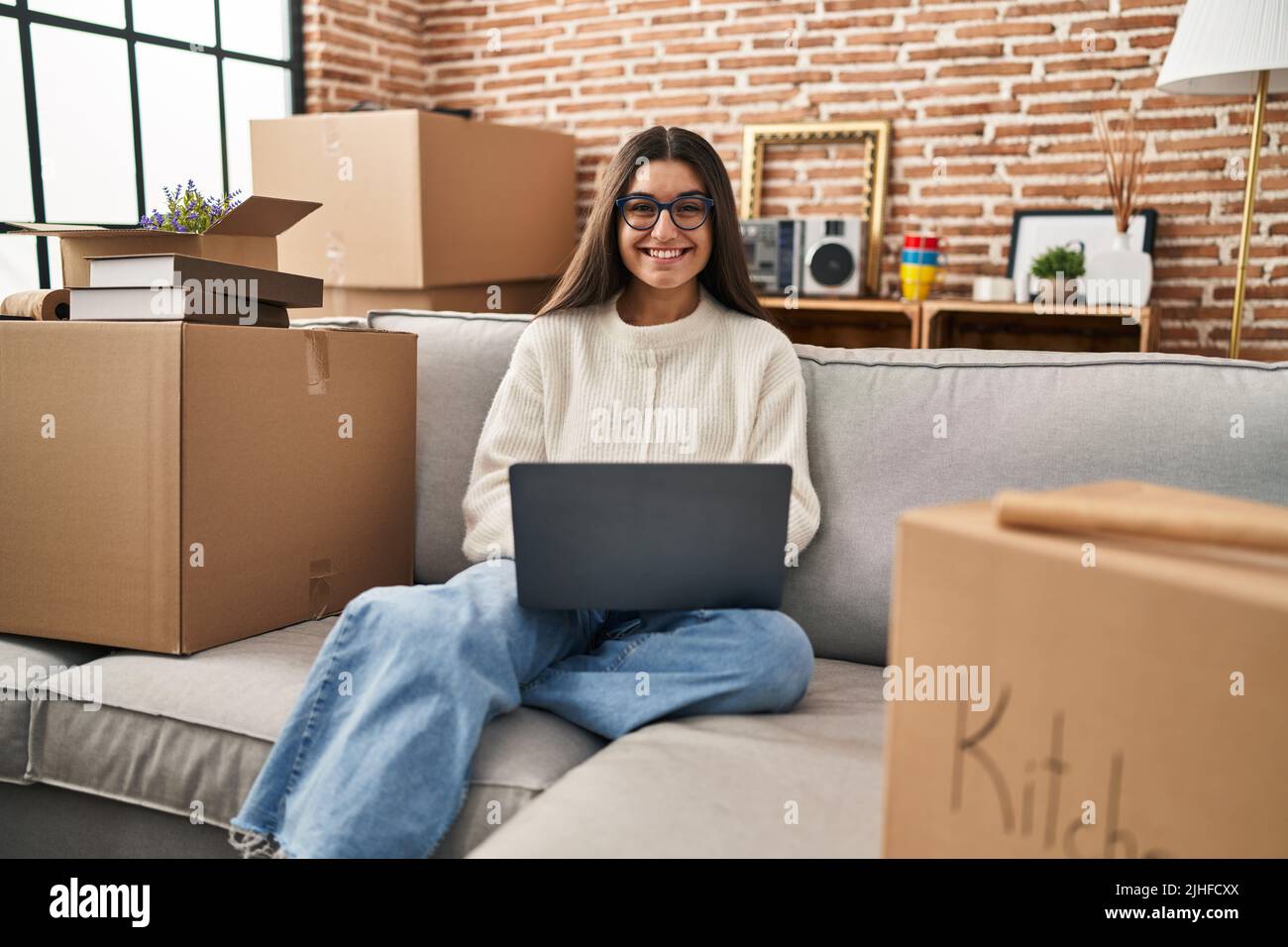 Young hispanic woman sitting on the sofa at new home using laptop ...