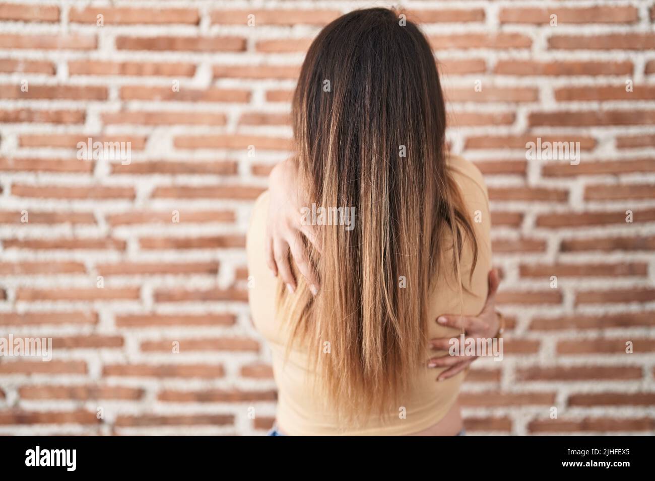 Young woman standing over bricks wall hugging oneself happy