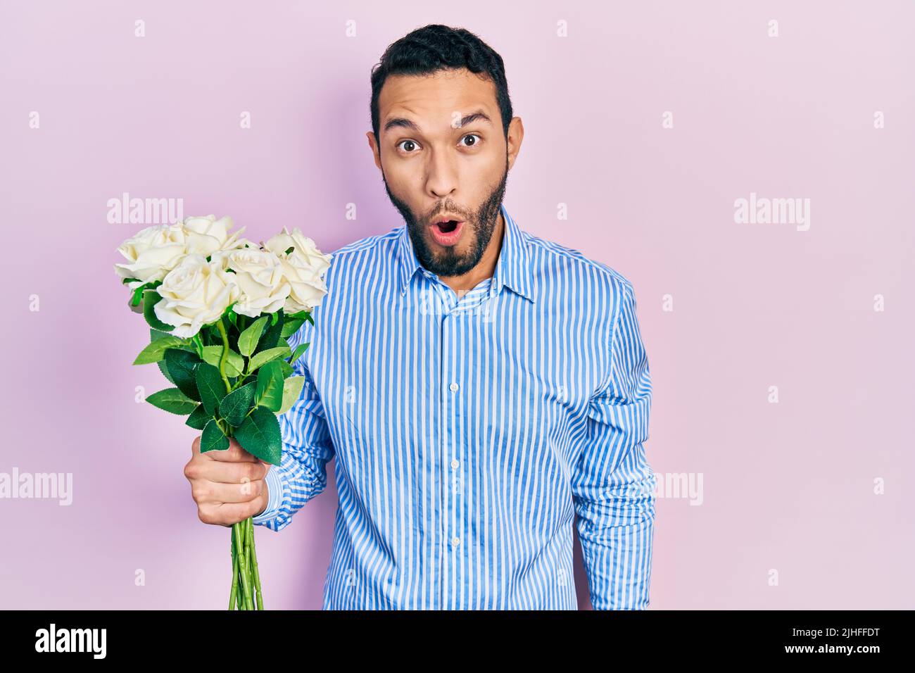 Hispanic man with beard holding bouquet of white flowers scared and ...
