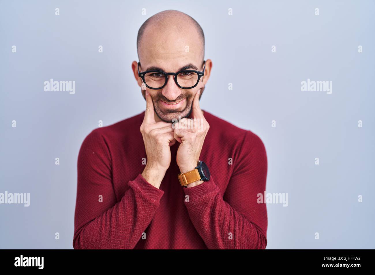 Young bald man with beard standing over white background wearing glasses smiling with open mouth, fingers pointing and forcing cheerful smile Stock Photo