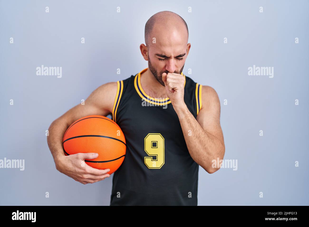 Young bald man with beard wearing basketball uniform holding ball