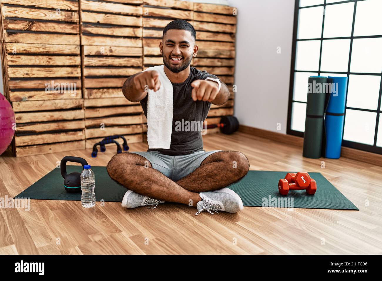young-indian-man-sitting-on-training-mat-at-the-gym-pointing-to-you-and