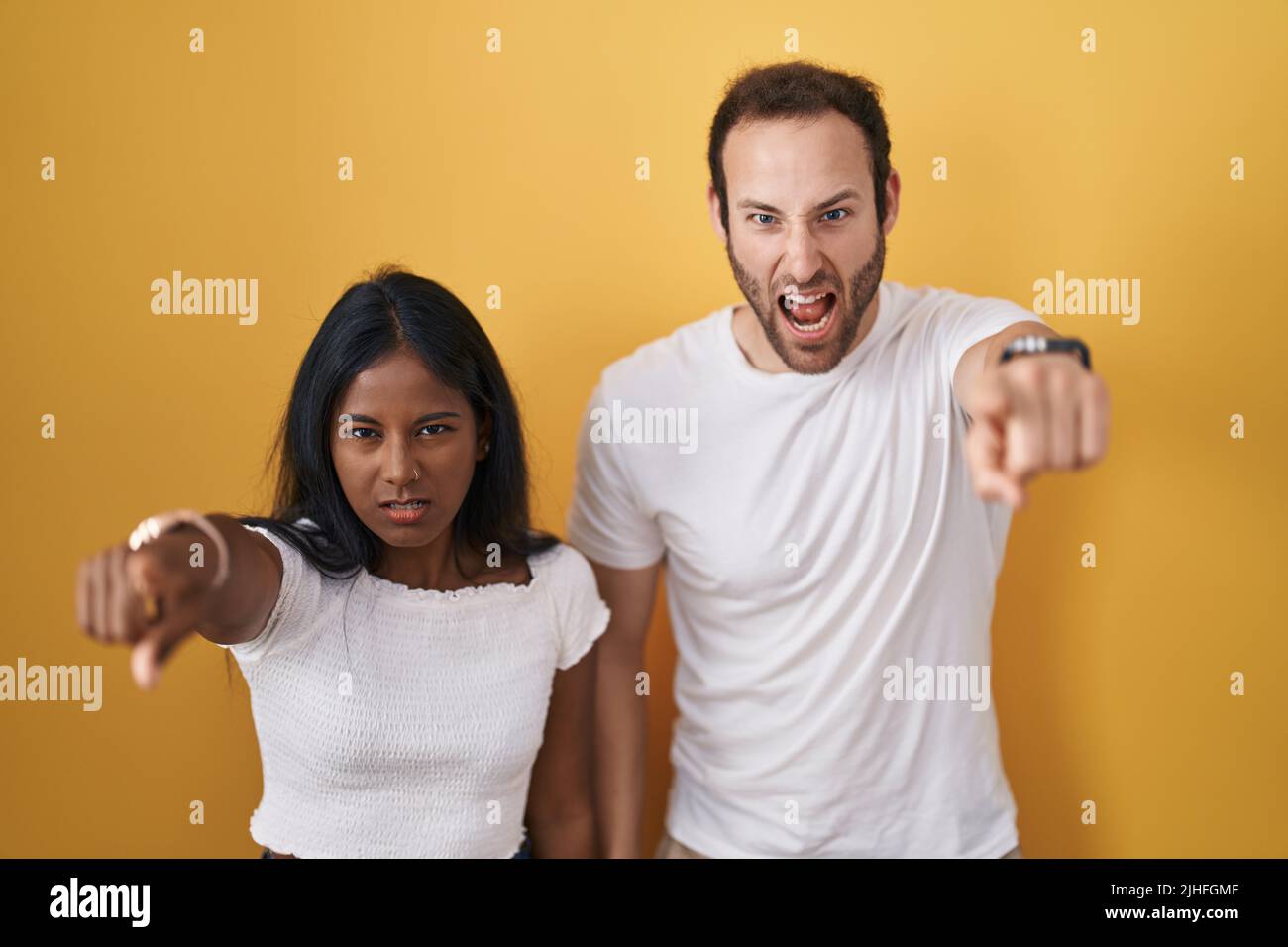 Interracial couple standing over yellow background pointing displeased ...