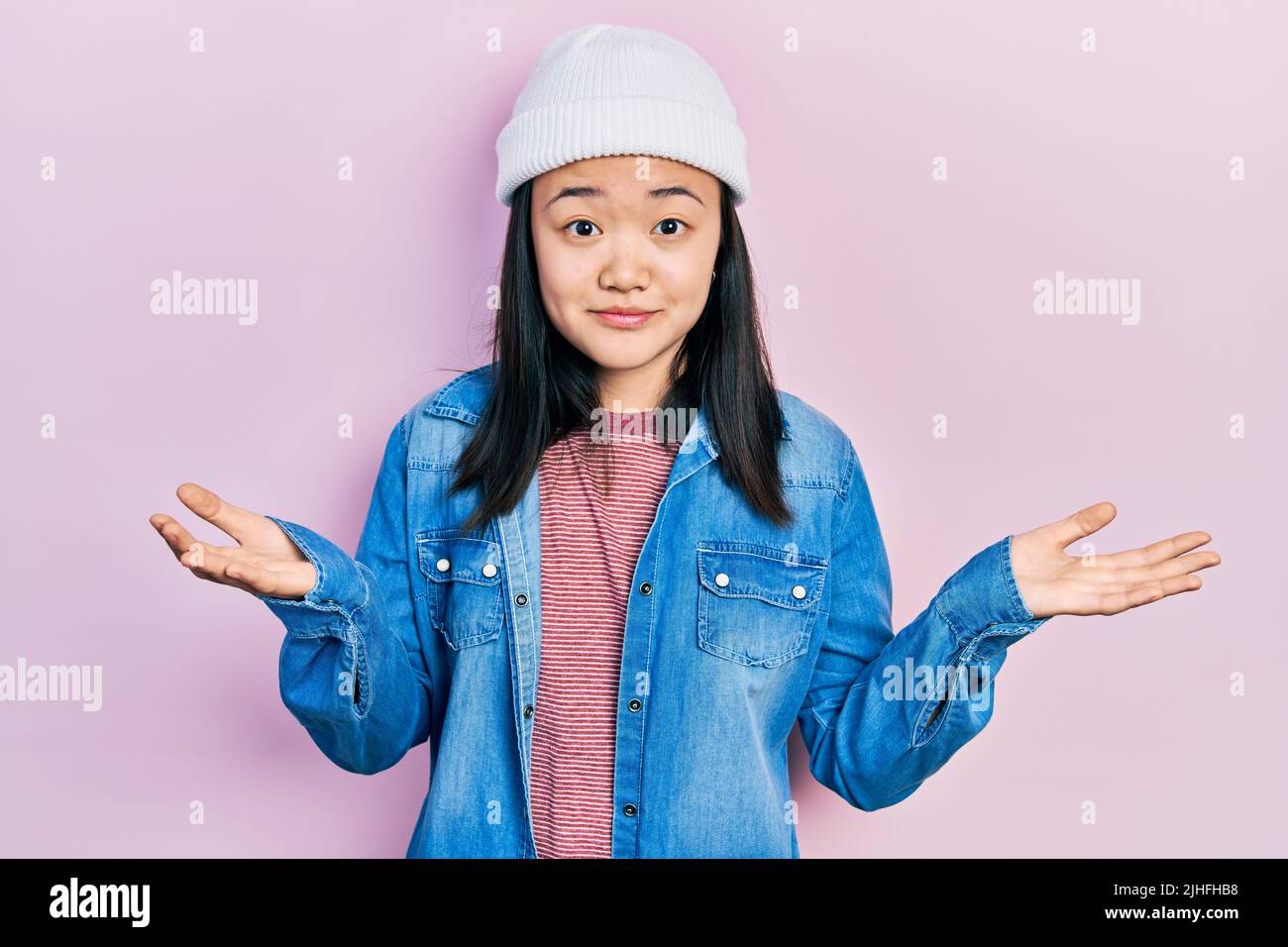 Young chinese girl wearing cute wool cap clueless and confused expression with arms and hands raised. doubt concept. Stock Photo