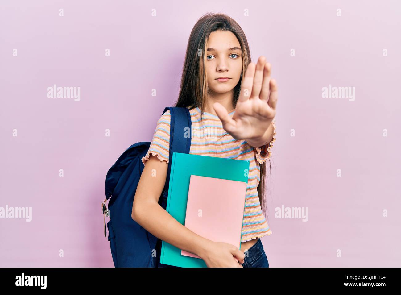 Young girl holding student backpack and books with open hand doing stop sign with