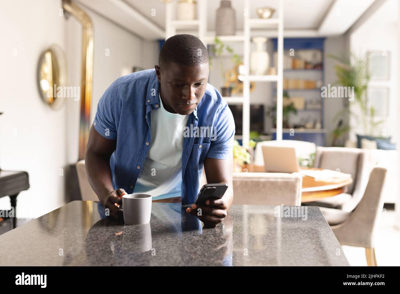 Vertical image of african american man drinking coffee and using smartphone Stock Photo