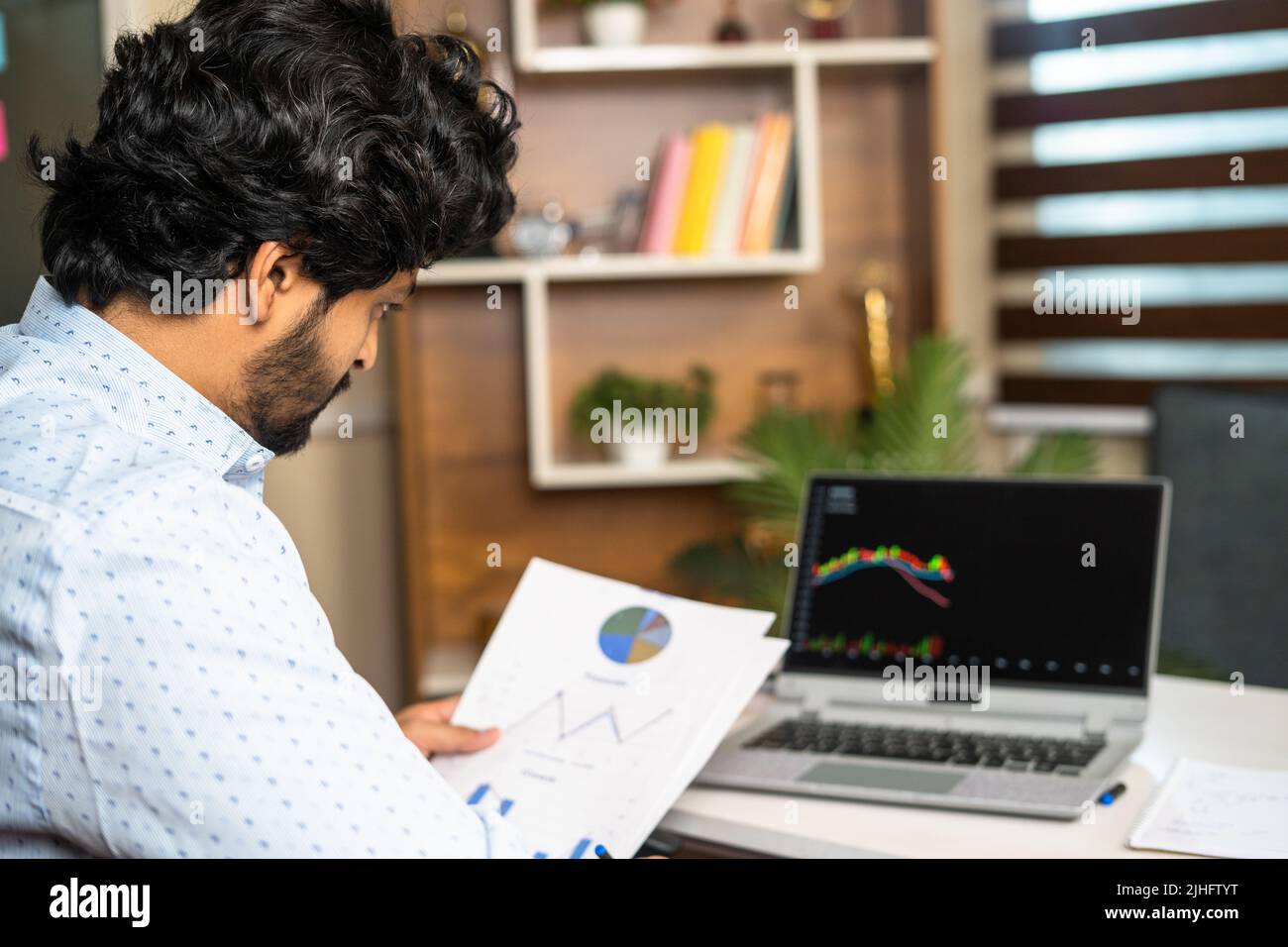 young man busy analysing Companies financial charts with technical stock mart charts on laptop - concept of investment, trading and money management Stock Photo