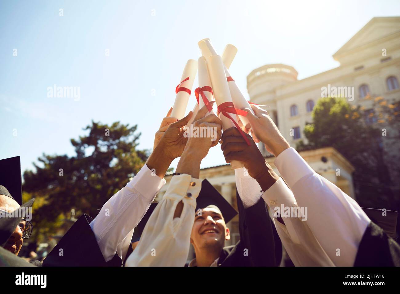 Happy university students holding up their diploma scrolls during graduation ceremony Stock Photo