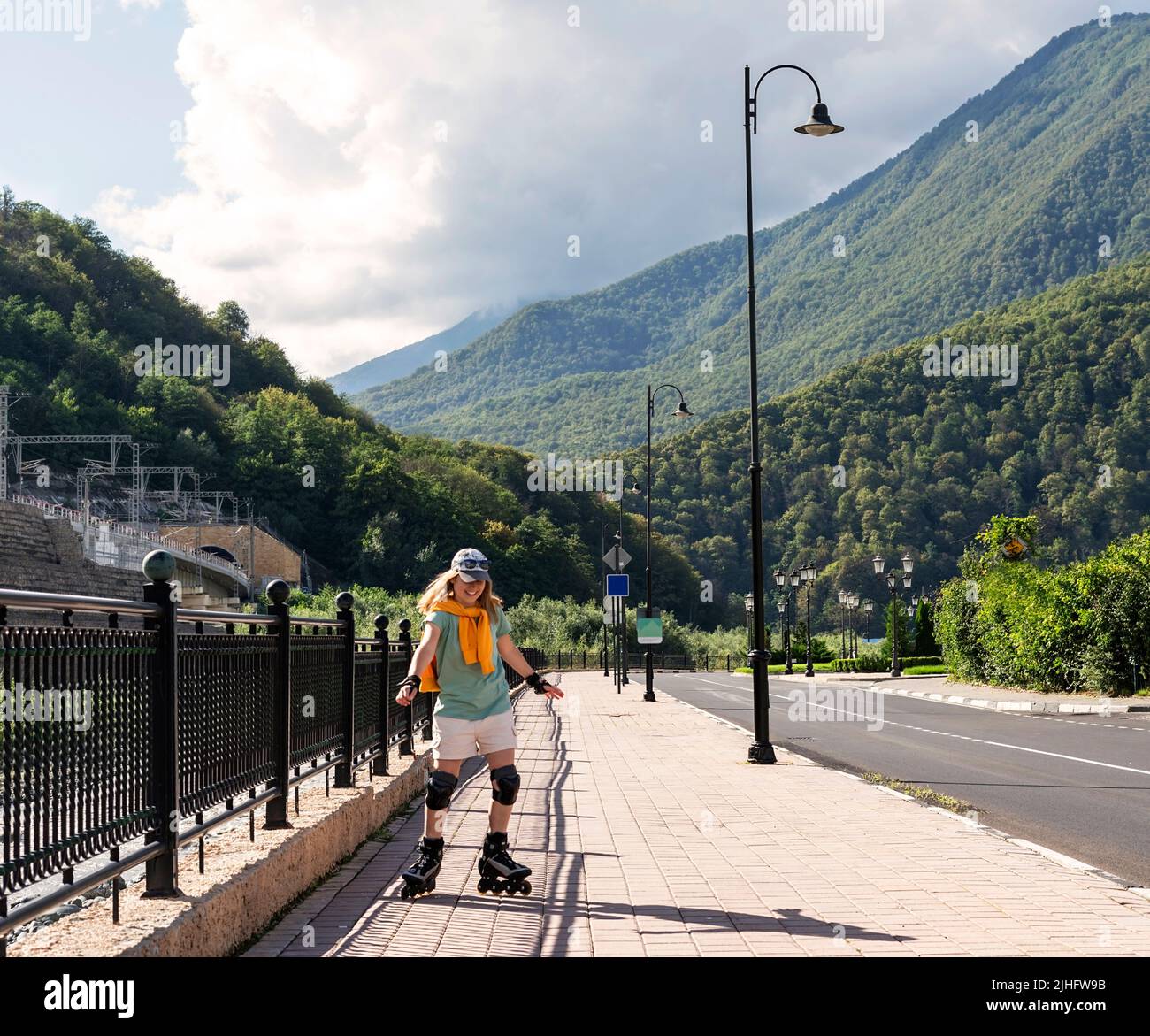 happy young woman in protective equipment riding on roller skates along embankment in summer active lifestyle, outdoor activities, roller skating Stock Photo