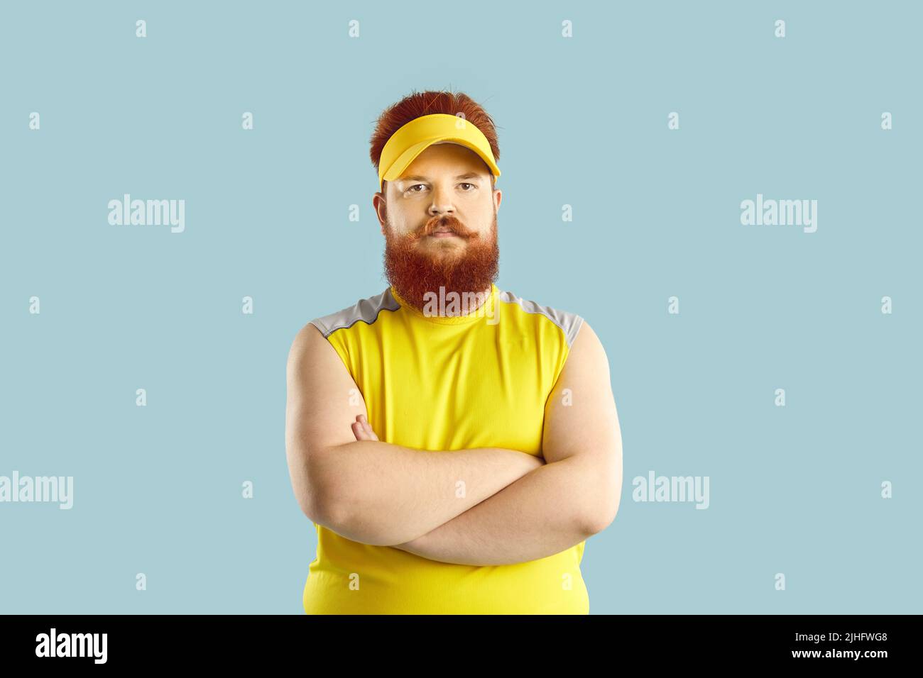 Angry displeased fat athlete standing with his arms crossed isolated on blue background Stock Photo