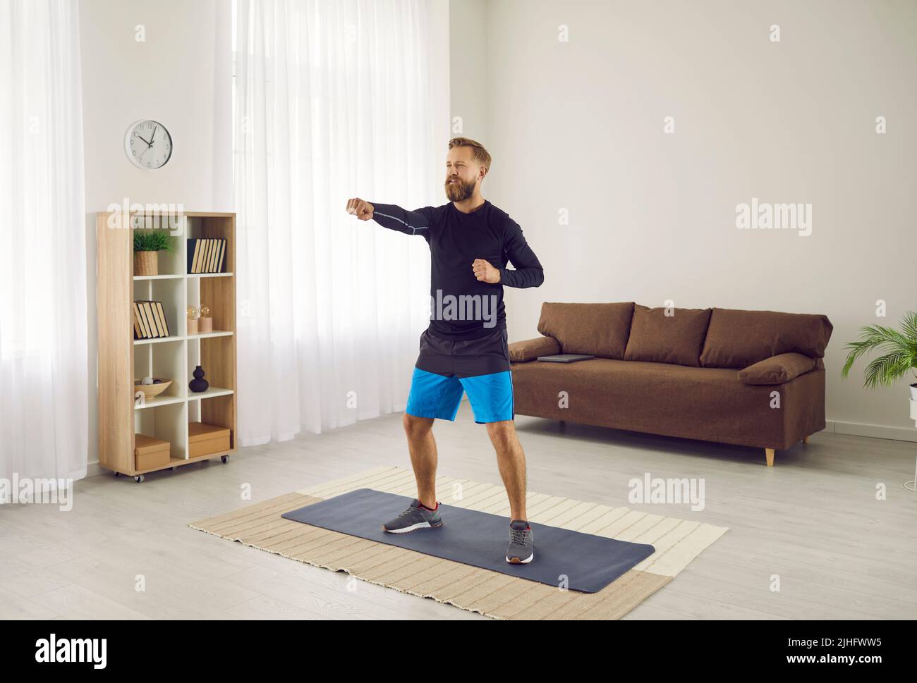 Athletic man does sports at home doing cardio workout with intense blows to air. Stock Photo