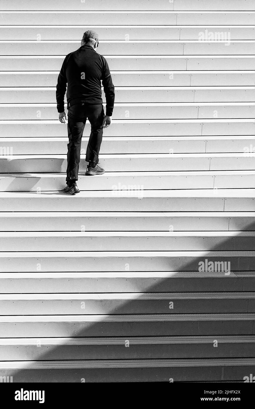 A grayscale of a man walking up the steps alone in the city Stock Photo