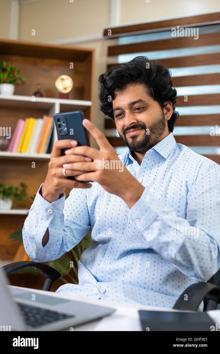 happy Young corporate employee busy using mobile phone at office in front of laptop at desk - concept of relaxation, taking break and social media Stock Photo