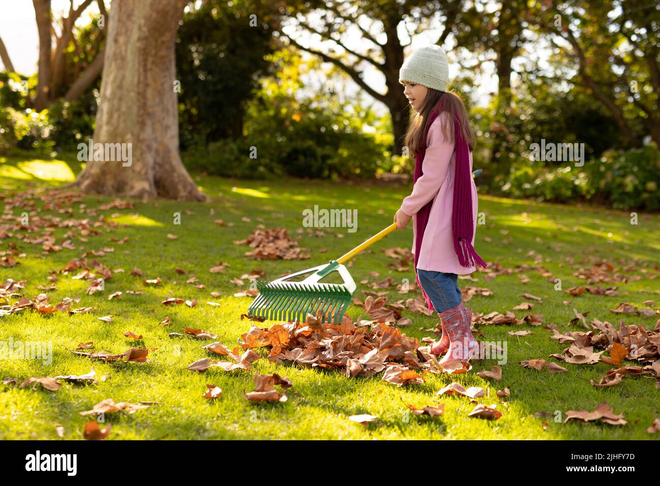 Image of happy caucasian girl swiping leaves in autumn garden Stock Photo