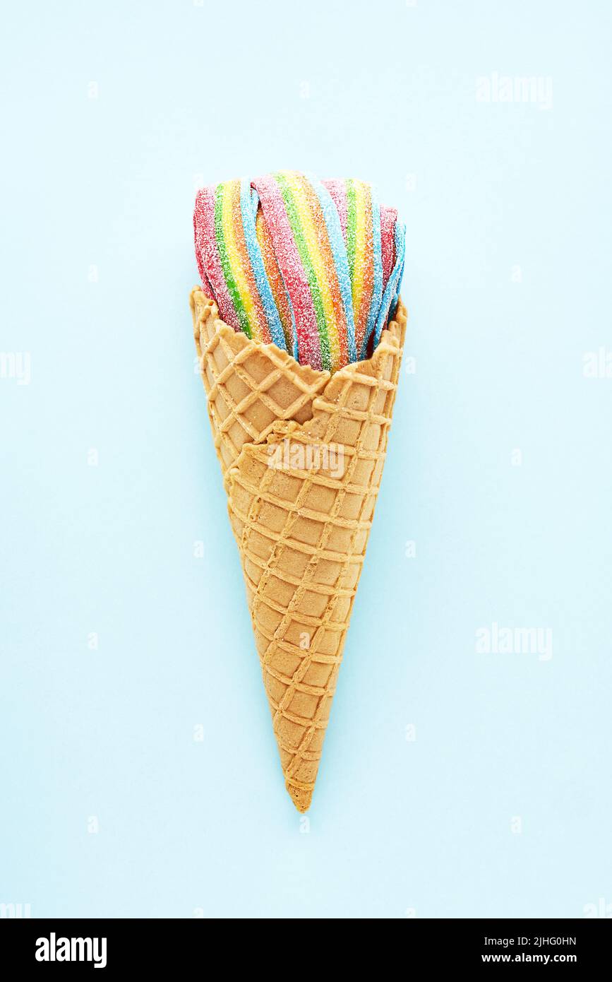 Colorful sour jelly candies in sugar sprinkles in an ice cream cone on a light blue background. Flat lay, copy space, vertical. Stock Photo