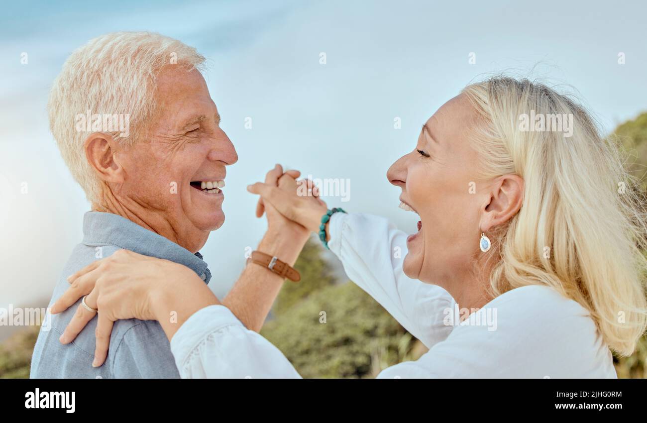 A happy mature caucasian couple enjoying fresh air on vacation at the beach. Smiling retired couple dancing outside Stock Photo