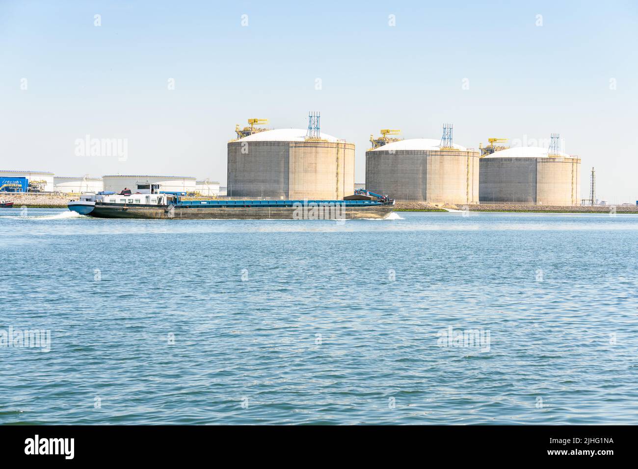 Bulk carrier barge in harbour with large concrete LNG taks in background. Port of Rotterdam, The Netherlands. Stock Photo