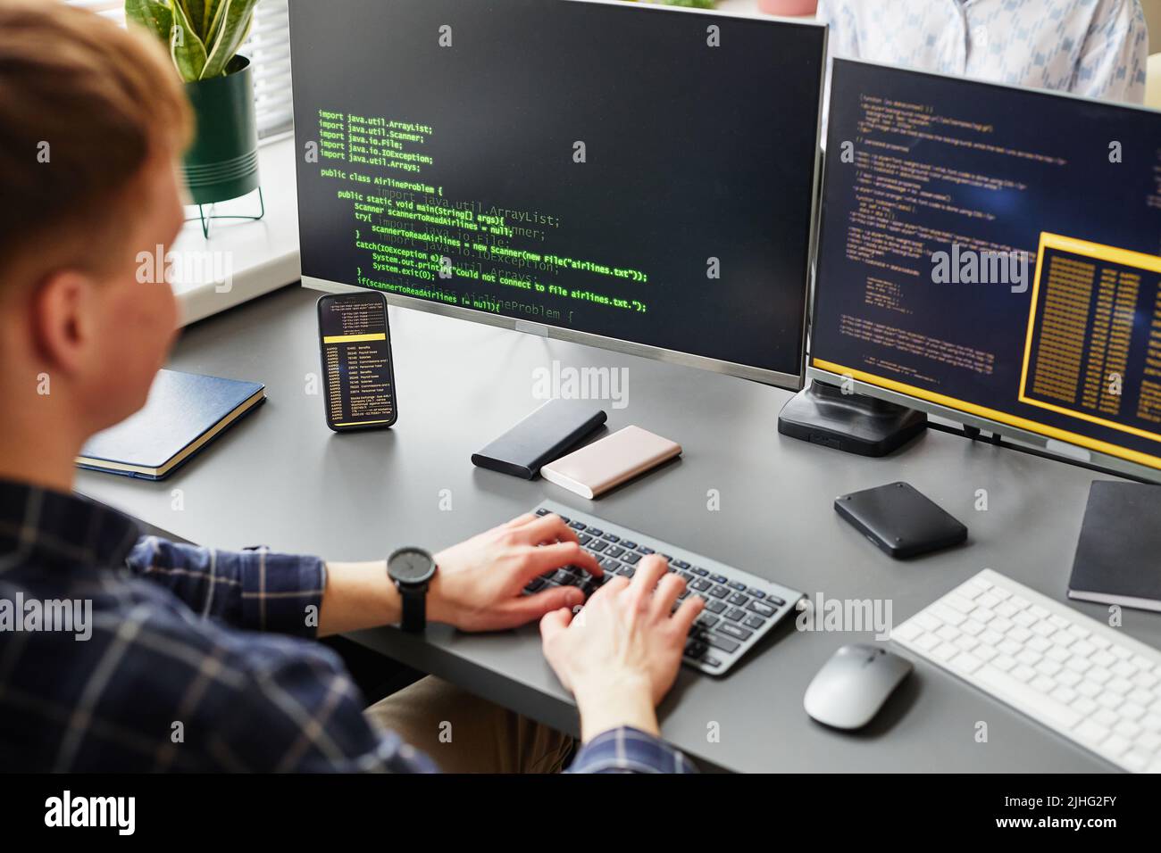 Rear view of young software developer writing codes of new software sitting at his workplace with computer monitors Stock Photo