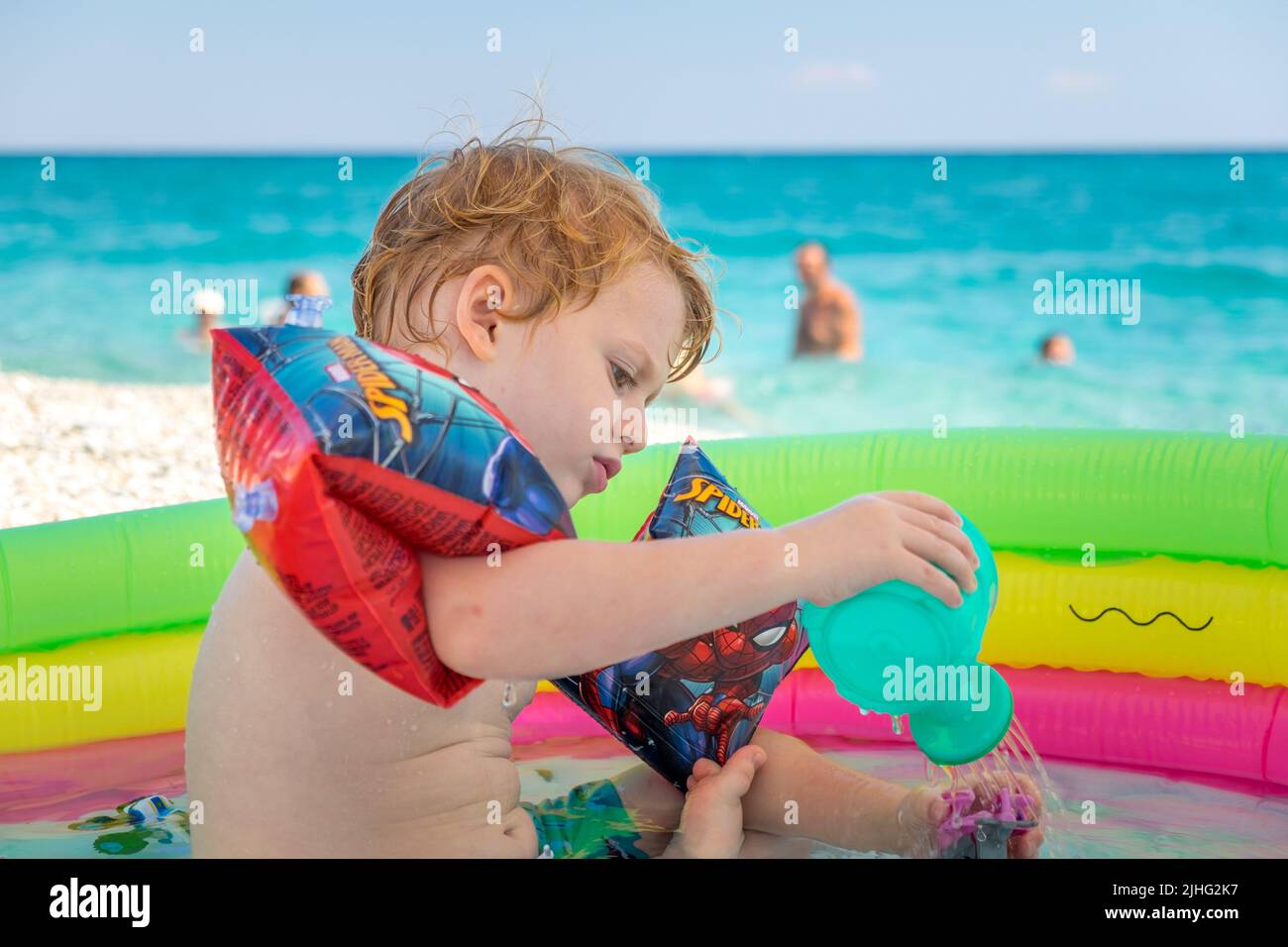 Cute little boy playing in his inflatable pool with his plastic ...