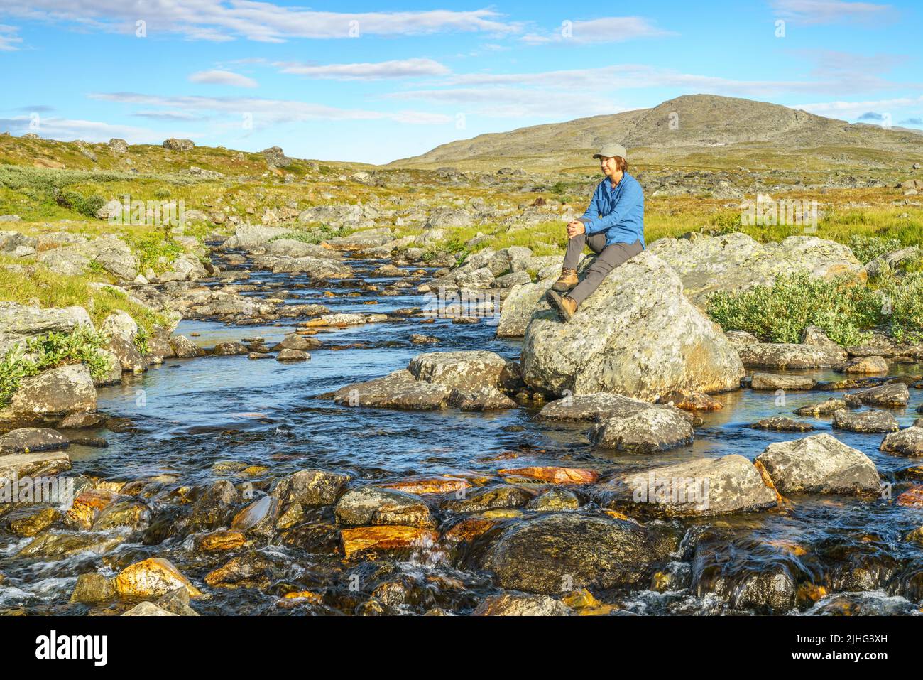 Woman sitting on a rock at a creek in mountain area along the kings trail,  Gällivare county, Swedish Lapland, Sweden Stock Photo