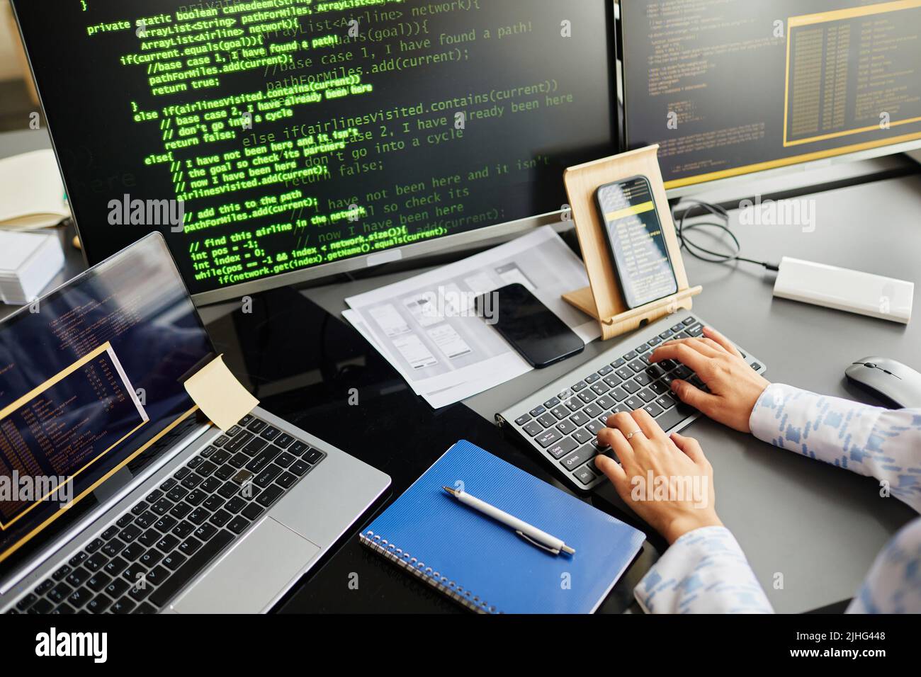 Close-up of IT worker developing new software on computer typing on keyboard and connecting smartphone and laptop with codes at her workplace Stock Photo