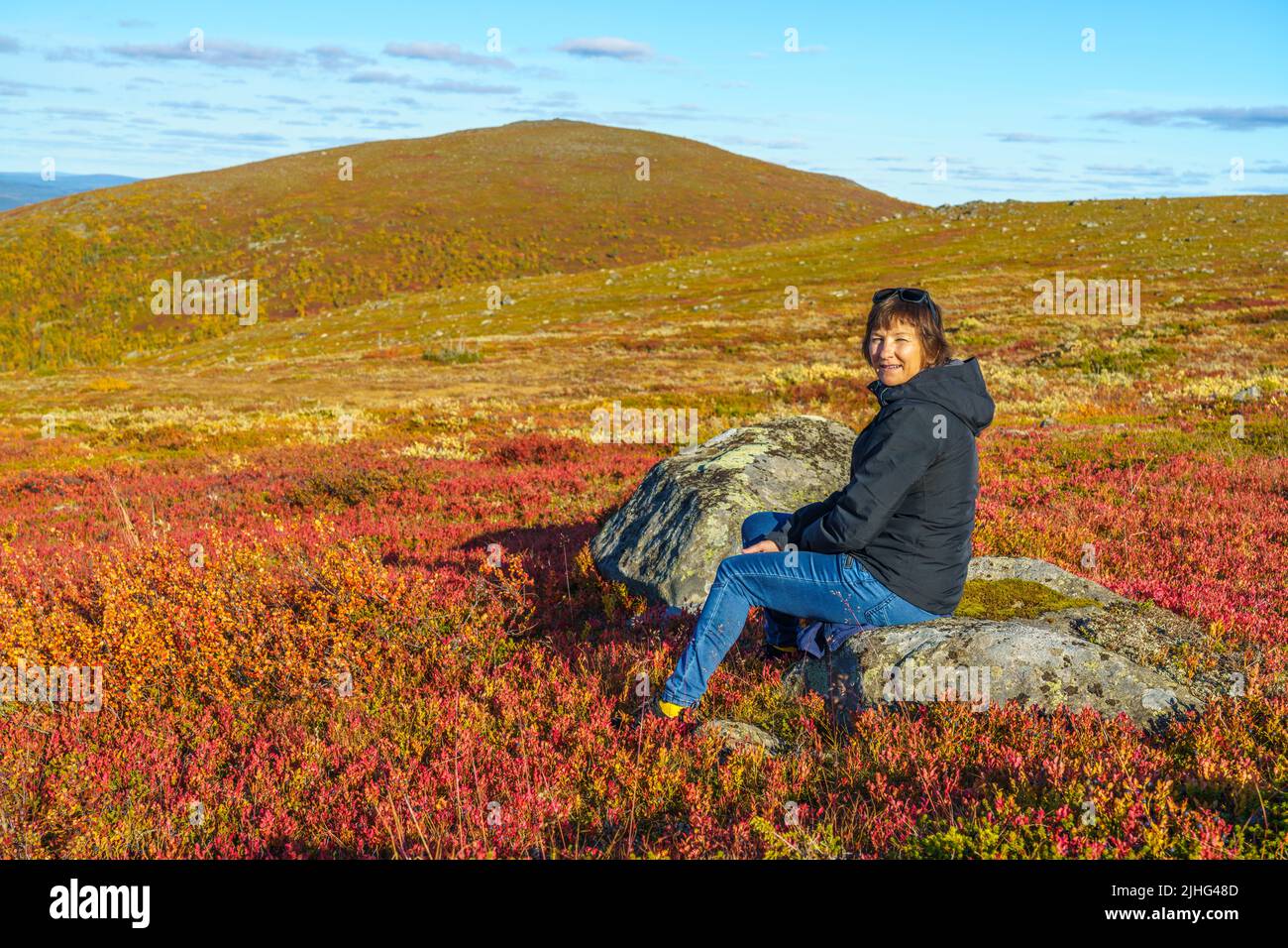 Woman sitting on a rock on Mount Dundret in autumn season with nice colors, Gällivare, Swedish Lapland, Sweden Stock Photo